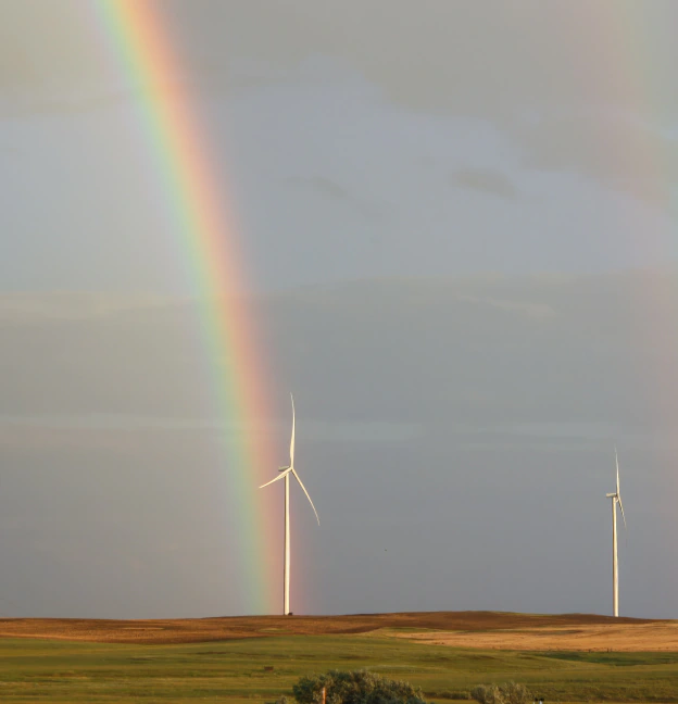Pastoral view of two wind turbines and rainbow.