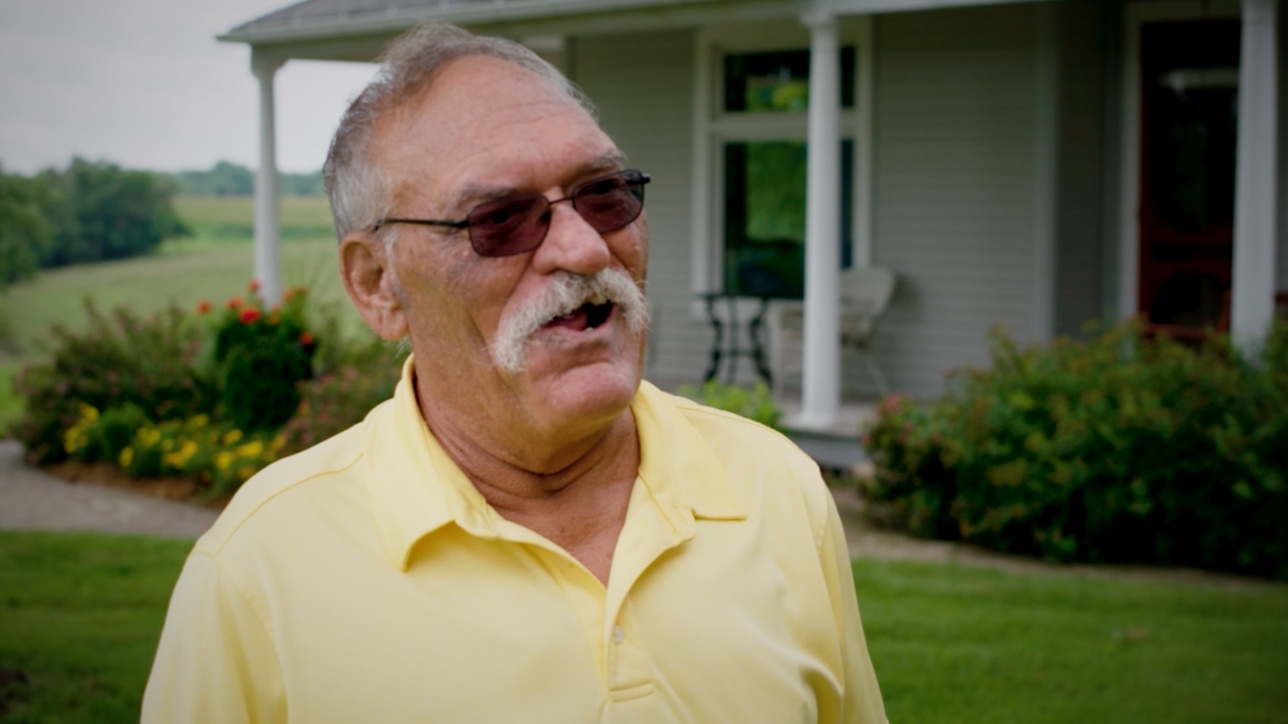 Man with sunglasses and mustache in front of house.