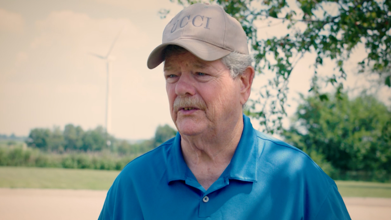 Man with baseball hat outside with singular wind turbine in the background